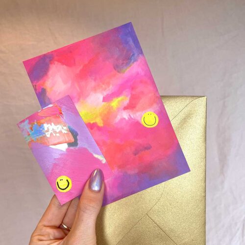 hand holding Colourful holographic vinyl sticker and abstract art print both with happy faces