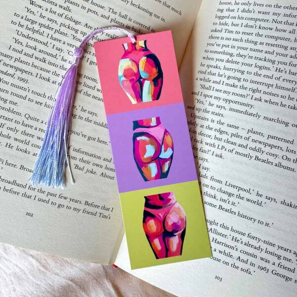 Colourful bums bookmark. One on peach, one on lilac and one on lime green. Bookmark has colourful tassel and is laid on an open book.