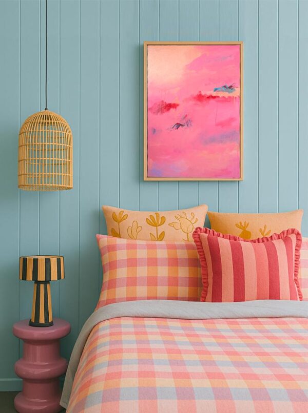 Pink red and blue abstract art above a pink and blue patterened bed with cushions