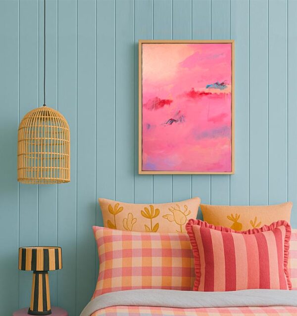 Pink red and blue abstract art above a pink and blue patterened bed with cushions