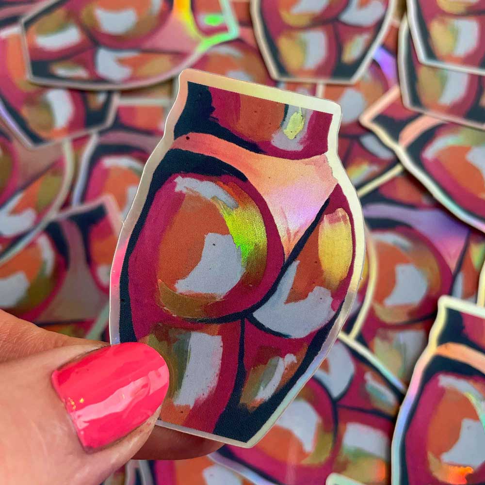 holographic butt sticker, held by a thumb with pink nail varnish surrounded by more holographic butt stickers
