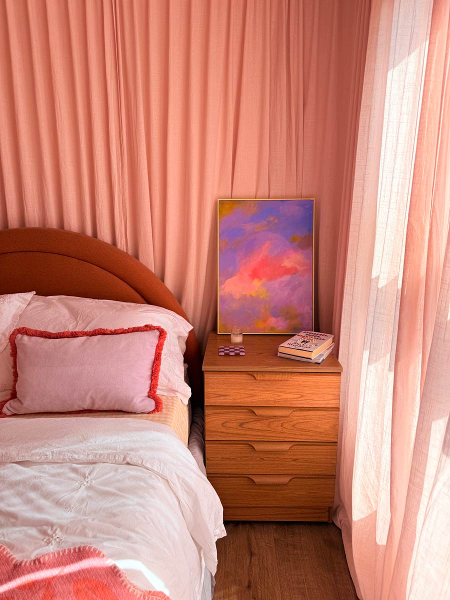 Bed with pink curtains around and moon painting on bedside table